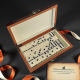 Отворена дървена кутия с метална закопчалка, пълна с класически бели плочки за домино с черни точки