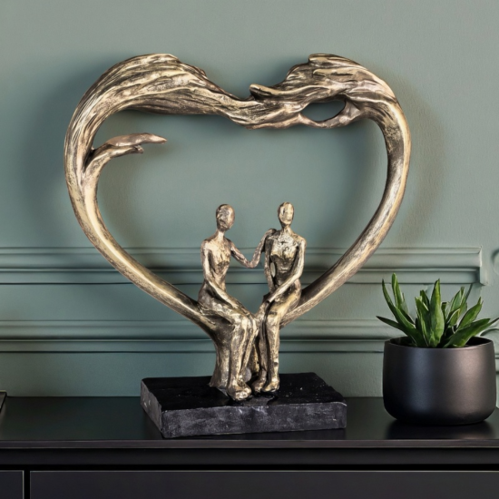 Арт скулптура с бронзов ефект, изобразяваща голямо сърце, образуващо арка над седяща двойка