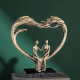 Арт скулптура с бронзов ефект, изобразяваща голямо сърце, образуващо арка над седяща двойка