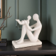 Бяла абстрактна статуетка от полирезин с ефект на камък, изобразяваща седнала майка, която е вдигнала детето си във въздуха в момент на игра