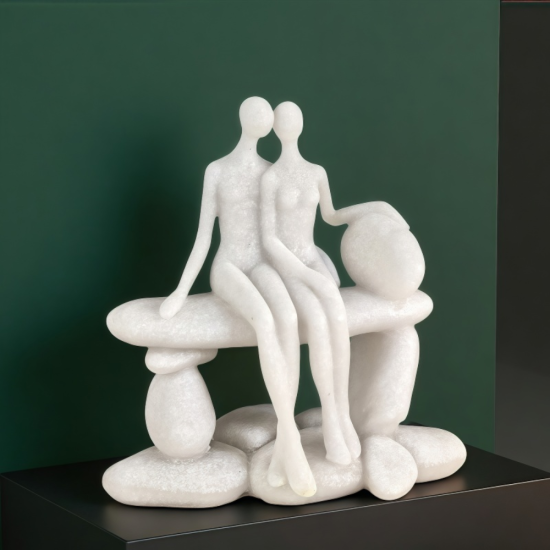 Бяла абстрактна статуетка от полирезин с ефект на естествен камък, изобразяваща влюбена двойка, седнала прегърната върху каменна пейка