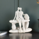 Бяла абстрактна статуетка от полирезин с ефект на естествен камък, изобразяваща влюбена двойка, седнала прегърната върху каменна пейка
